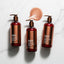 Copper peptide shampoo bottles arranged on clean white surface with copper-tinted droplets