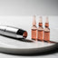At-home hair mesotherapy pen device and copper peptide serum vials on white marble surface